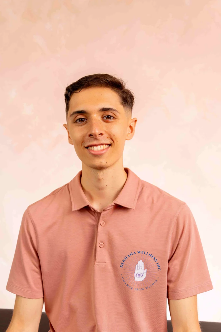 Jordan Curcio smiling in a pink polo shirt with Dekhana Wellness Inc. logo, showcasing his role as a personal trainer and holistic health coach focused on alignment-based movement and body awareness.