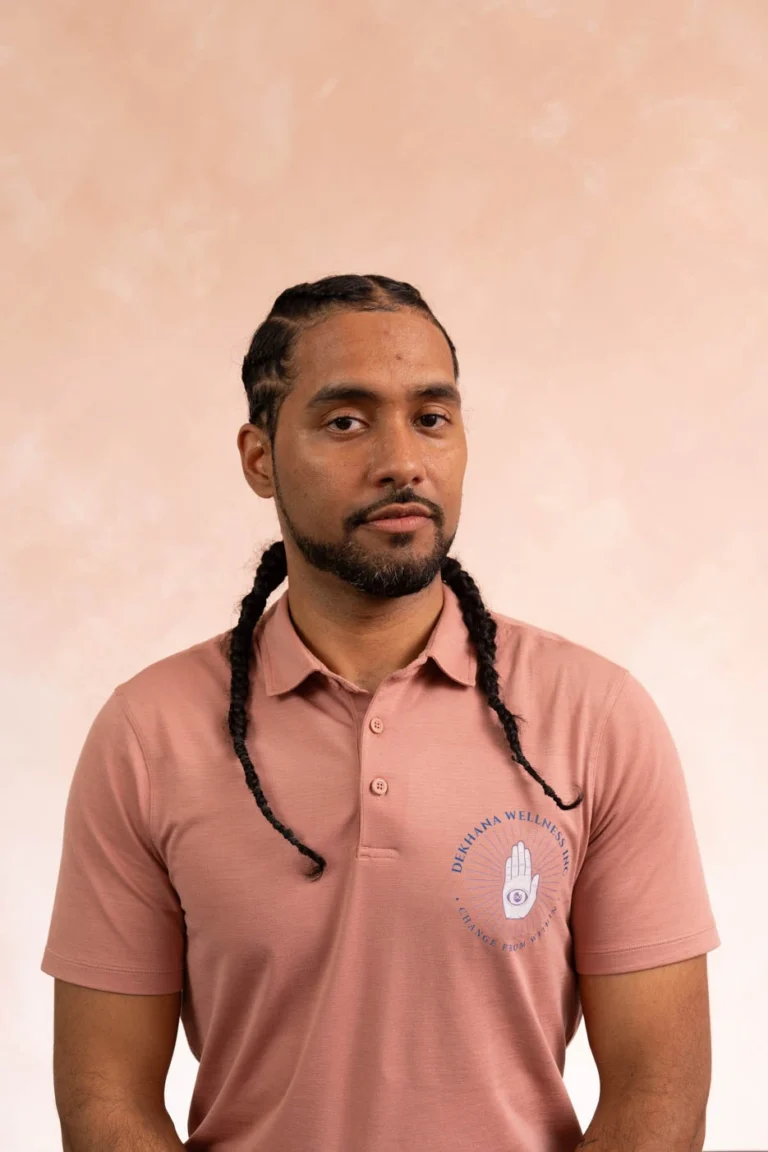 Kenny Gangji, wellness professional at Dekhana Wellness Inc., wearing a pink polo shirt with logo, showcasing a confident expression against a soft pastel background.