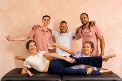 Five people posing on a black surface against a pink wall, smiling and dressed in casual clothing.